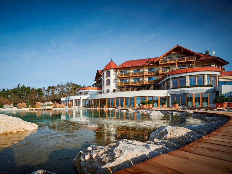Die Außenansicht Hotel Der Birkenhof mit Badeteich im Vordergrund.