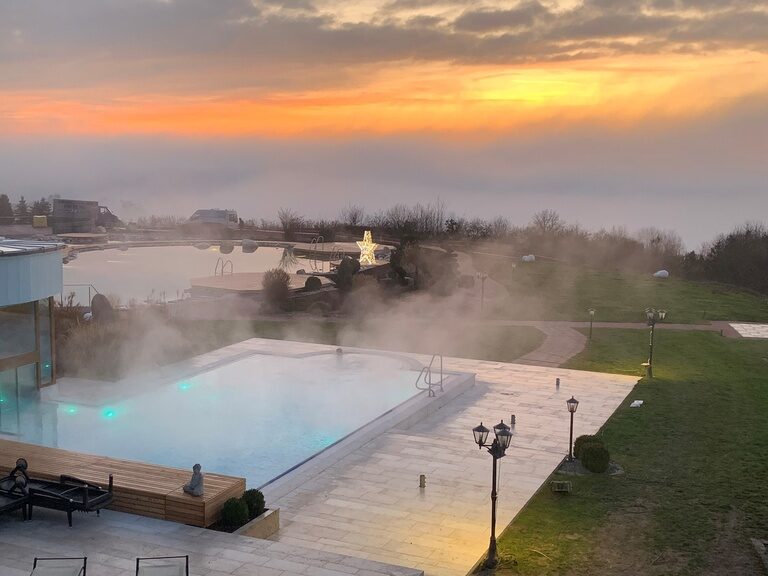 Warmer, dampfender beleuchteter Aussenpool des Wellnesshotels der Birkenhof beim Bayerischen Wald in der Abenddämmerung.