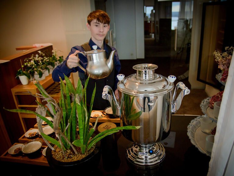 Der Azubi mit Teekanne am Tee-Buffet während der Frühstücksvorbereitungen im Hotel Der Birkenhof.