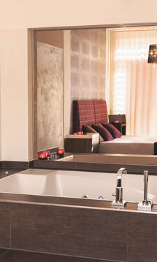 Badewanne mit Blick auf das Doppelbett durch einen Spiegel