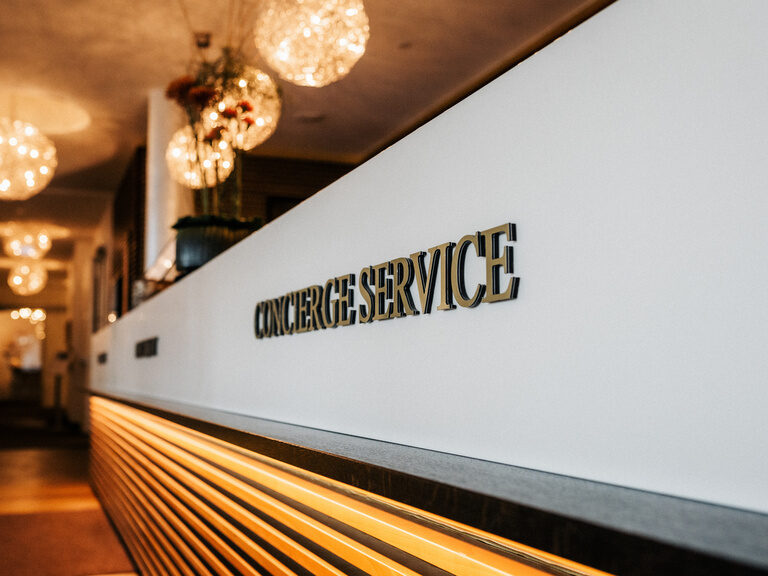 Der moderne Empfangsbereich mit Schriftzug und gedimmter Beleuchtung des Wellnesshotel Der Birkenhof in der Oberpfalz.