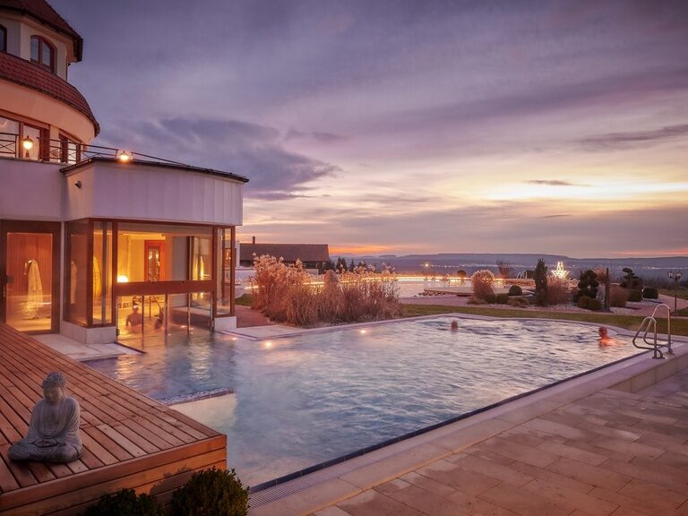 Der große Outdoor-Pool im Wellnesshotel der Birkenhof in der Oberpfalz bei Abenddämmerung.