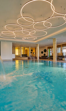 Das elegante Hallenbad mit einem zentralen Wasserfall im Wellnesshotel Der Birkenhof in der Oberpfalz.