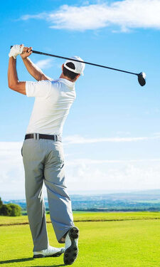 Ein Mann beim Golfschwung auf einem Golfplatz unter strahlend blauem Himmel.