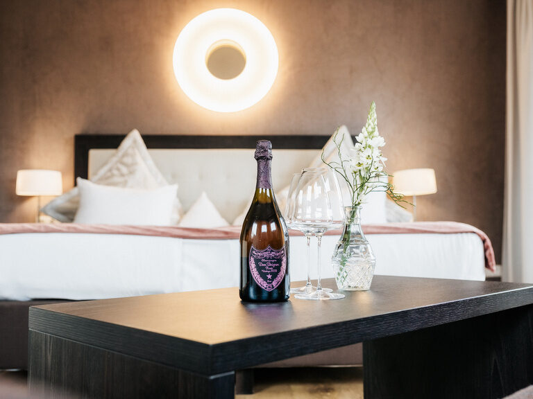 Das Bett mit eleganter Bettwäsche im De Luxe Doppelzimmer Seeblick mit einer Flasche Champagner als kleine Aufmerksamkeit des Hotels.