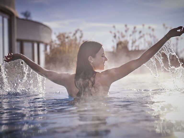 Eine Frau spielt mit dem Wasser des beheizten Außenpool im Wellnesshotel Der Birkenhof in Bayern.