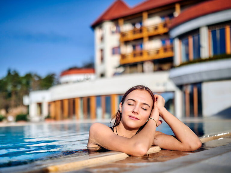 Die Frau genießt im beheizten Außenpool die warmen Sonnestrahlen.