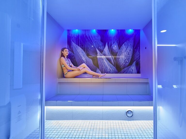 Die Frau sitzt im blau beleuchteten Dampfbad des Wellnesshotel Der Birkenhof in der Oberpfalz.