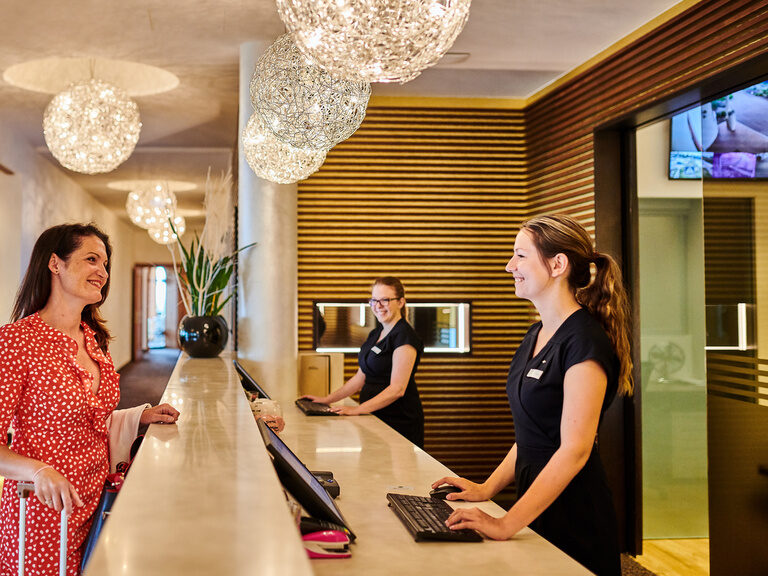 Ein Gast wird in der stilvollen Hotelrezeption des Hotels der Birkenhof in der Oberpfalz von freundlichem Personal begrüßt.