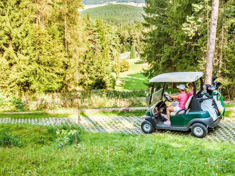 Ein Golfer genießt eine entspannte Fahrt im Golfwagen durch die grünen Landschaften eines Golfplatzes in der Nähe des Hotels der Birkenhof in der Oberpfalz.