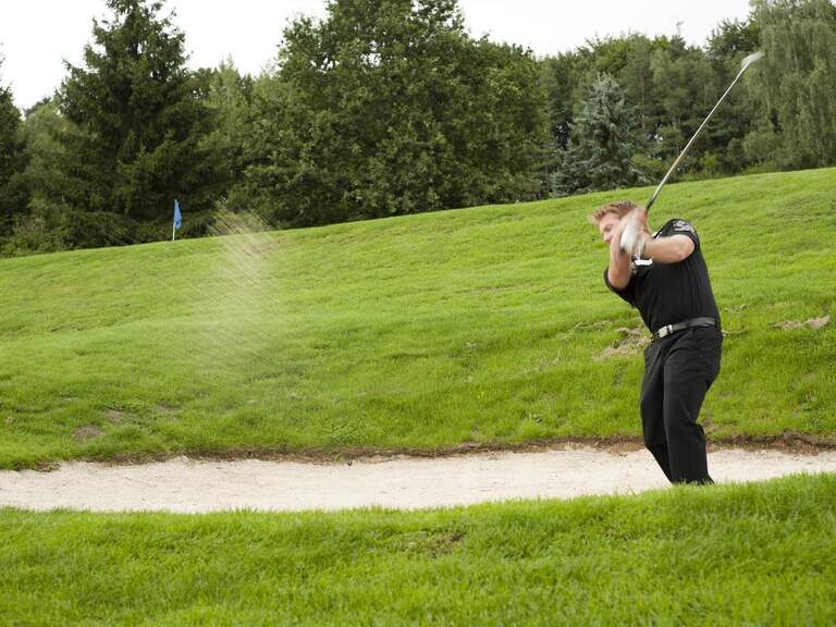 Der Golfer im Sandloch des Golfplatzes wirbelt beim Schlag Sand auf.
