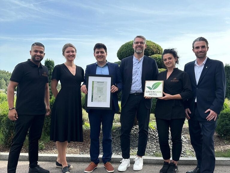 glückliches Hotelteam mit Greensign Auszeichnung in den Händen in der Gartenanlage des Hotels der Birkenhof in der Oberpfalz , das soziale Verantwortung und Nachhaltigkeit zeigt.