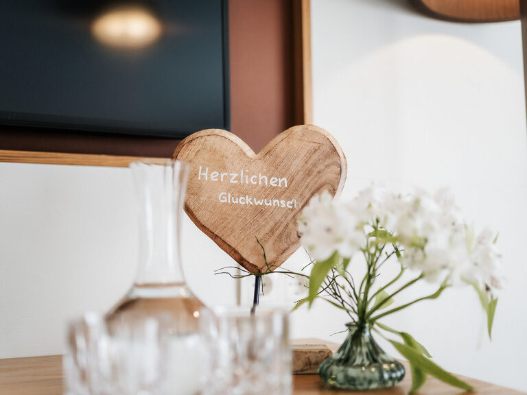 Ein Herz aus Holz und Blumen als Tischdekoration in der Mitte eines Zimmers des Hotels der Birkenhof beim Bayerischen Wald.