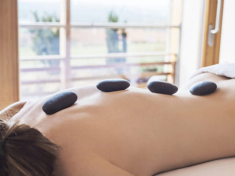 Ruhe und Erholung mit heißen Steinen für eine Frau auf einer Liege im Wellnesshotel der Birkenhof in Bayern.