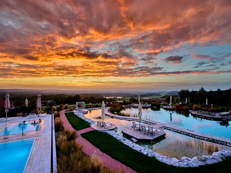Der weitläufige Hotelgarten mit Naturbadeteich und Aussenpool des Hotel Der Birkenhof im Bayerischen Wald, bei Sonnenuntergang.
