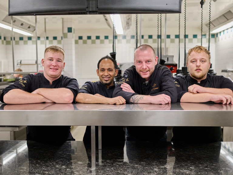 Das Kochteam in Kochbekleidung posiert in der Küche des umweltbewussten Hotels der Birkenhof in der Oberpfalz.