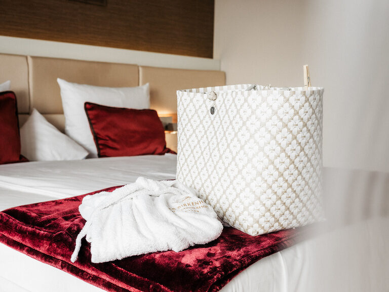 Gemütliches Bett mit weißen Laken und roten Kissen im Komfort Doppelzimmer des Hotels der Bikenhof in Bayern.