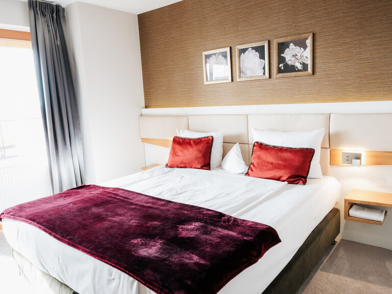 Ein großes komfortables Bett mit roten Kissen im Komfort Doppelzimmer des Hotels der Birkenhof in Bayern.