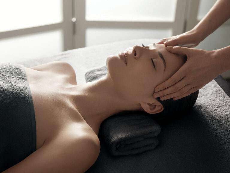 Liegende Frau bekommt eine entspannende Kopfmassage im Beauty- & Wellnessbereich in Bayern