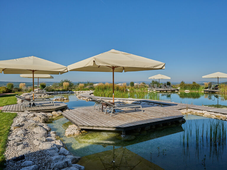 Das Holzpodest mit Sonnenschirmen am malerischen Natur-Badeteich des Wellnesshotel der Birkenhof im Bayerischen Wald.