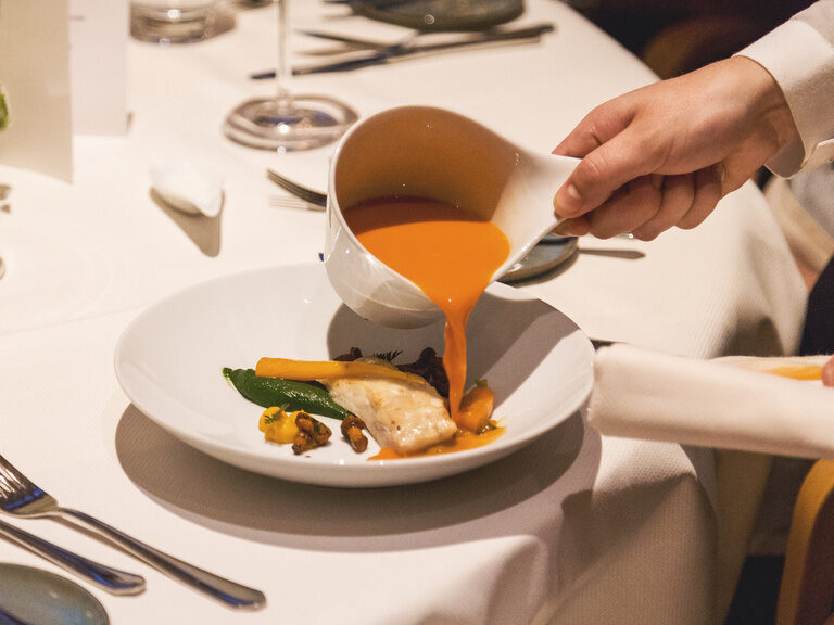 Ein weißer Porzellan Teller mit einer kulinarischen Spezialitäten aus dem Gourmetrestaurant Eisvogel in Bayern, serviert als Mittelpunkt des Settings.