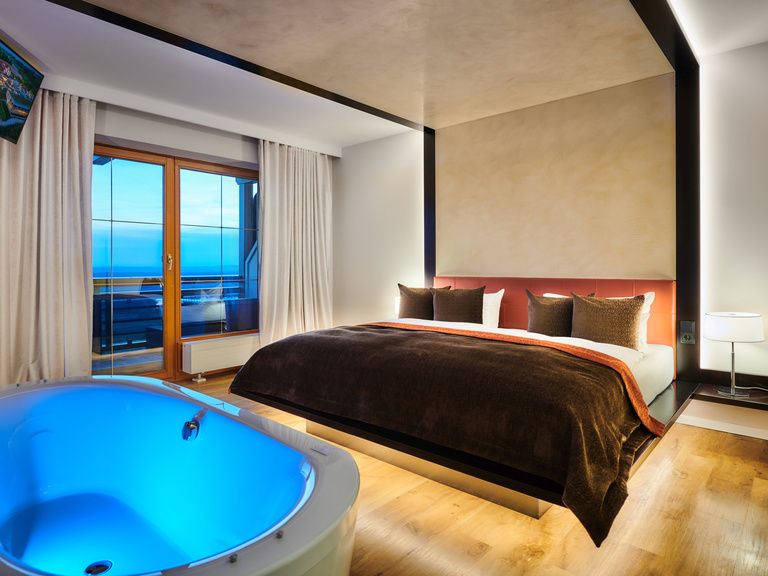 Schlafzimmer der First Suite mit blau beleuchteter freistehender Badewanne