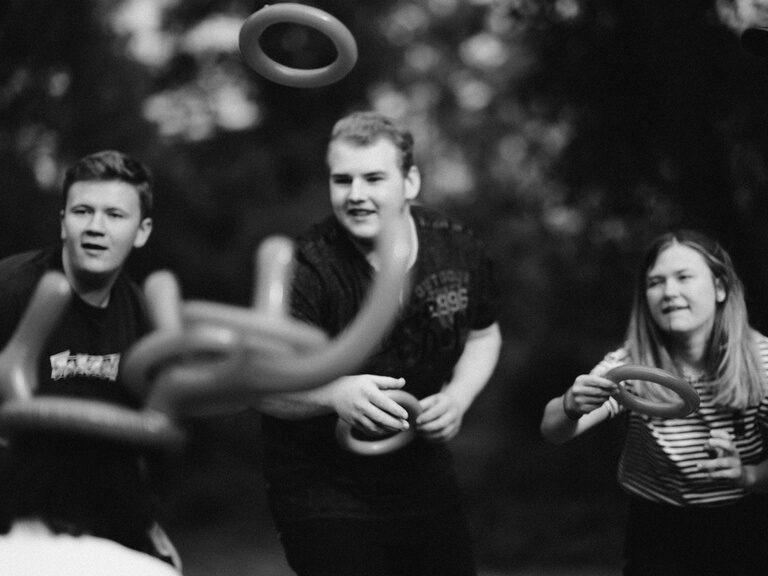 Ein Schwarz-Weiß-Foto einer Gruppe von Mitarbeitern des Hotels der Birkenhof in der Oberpfalz, die gemeinsam Zeit beim Ringe werfen verbringen als Zeichen der sozialen Nachhaltigkeit.