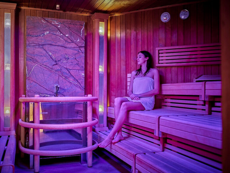 Violette Beleuchtung schafft eine entspannende Atmosphäre für eine Frau im wärmenden Tepidarium des Wellnesshotels der Birkenhof.